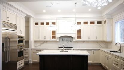 Completed white Traditional kitchen with detailed cabinet fronts, crown moulding, glass display cabinetry, and a dark island.